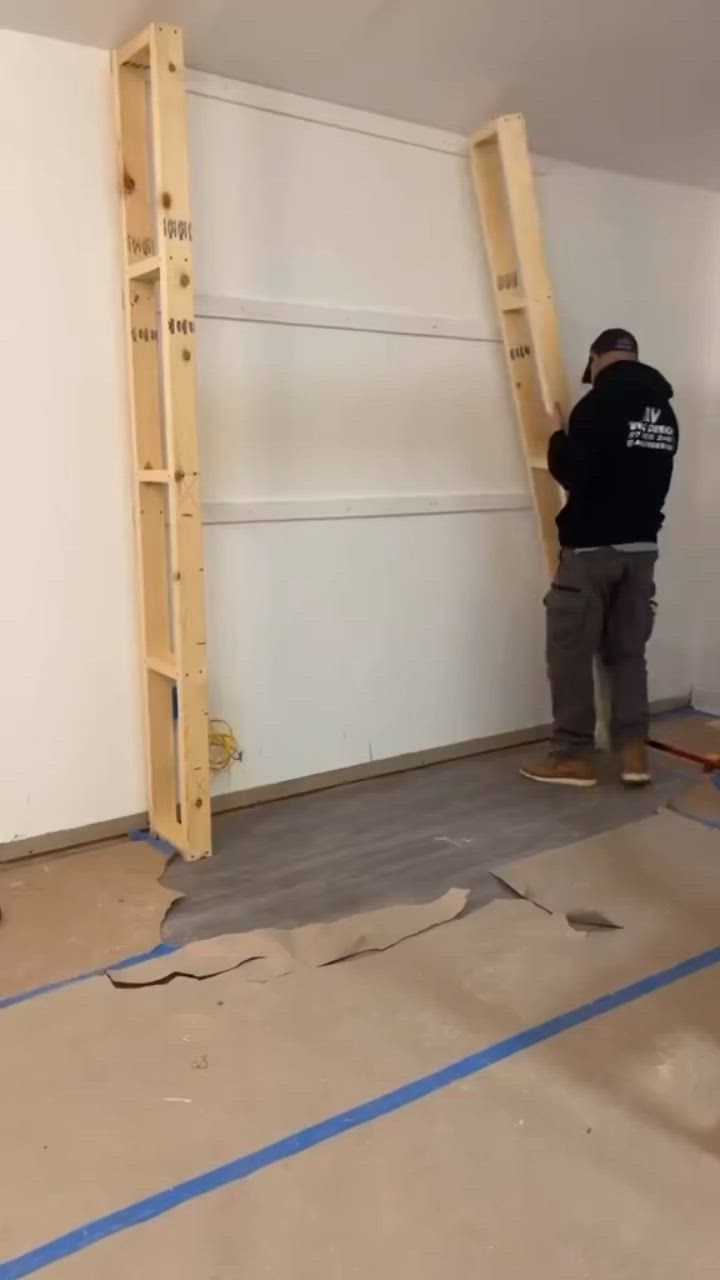 This may contain: a man standing next to a ladder in a room with white walls and blue tape on the floor