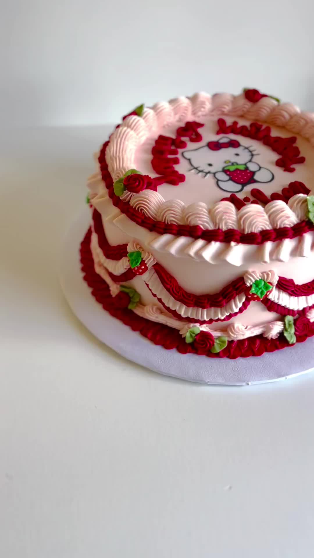 This may contain: a hello kitty cake with pink frosting and green leaves on it's edges