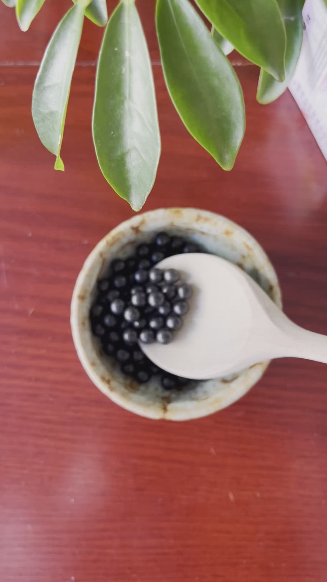 This may contain: a spoon with some blackberries in it on a table next to a potted plant