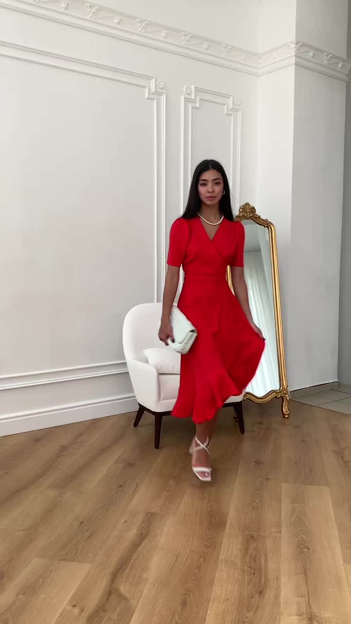 This may contain: a woman standing in front of a mirror wearing a red dress and holding a white purse