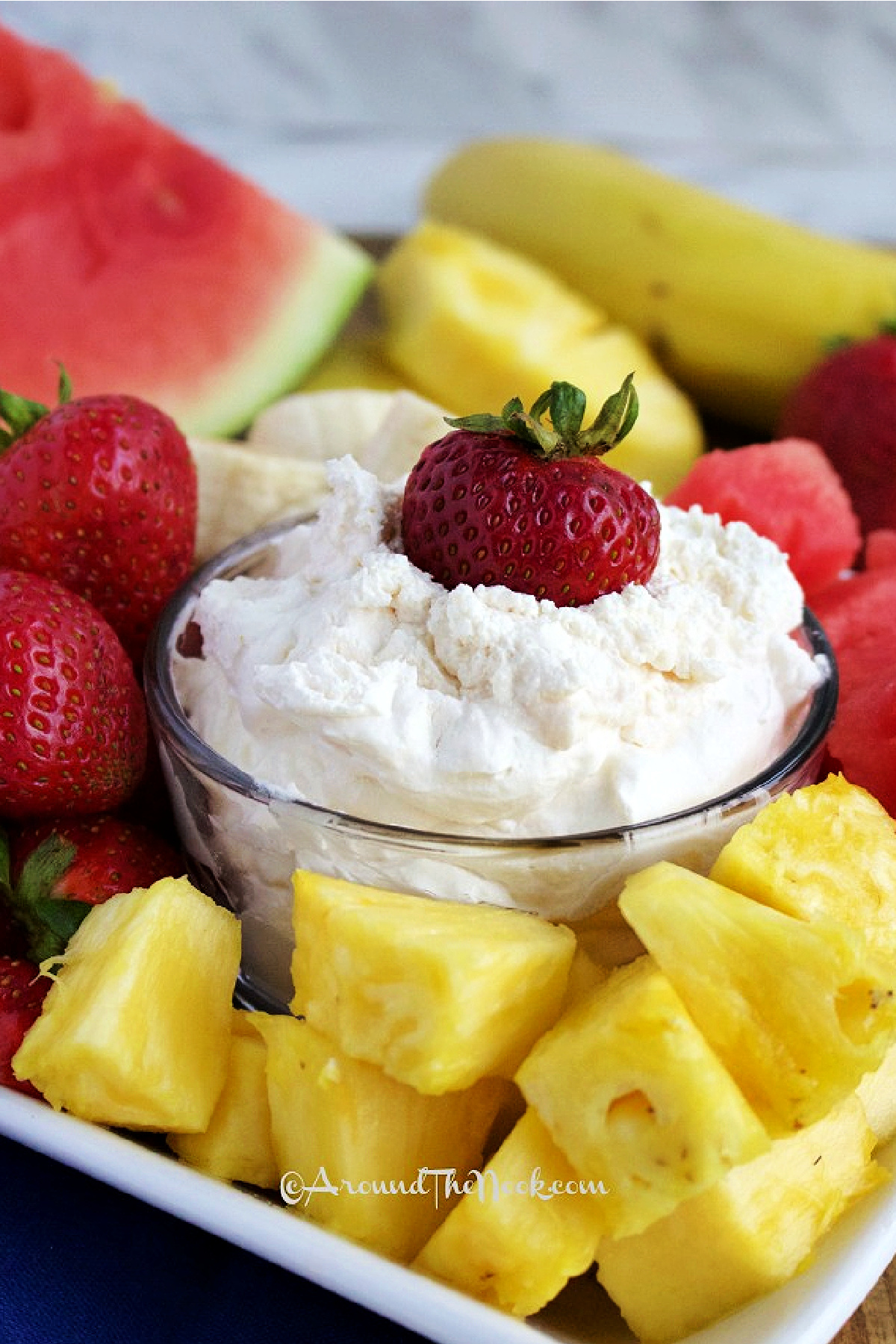 a platter of fruit with easy fruit dip in a clear bowl in the center, with a strawberry in it