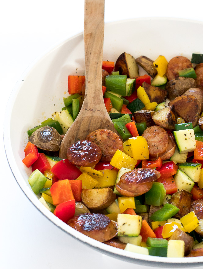 One Pan Sausage and Vegetables in a white skillet with a wooden spoon.