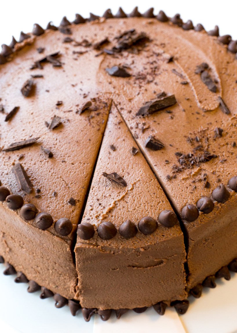 slicing chocolate cake topped with chocolate chips and chocolate shavings 