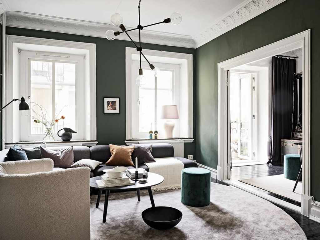 A dark green wall color in a living room with white window frames, door frames and white ceiling mouldings