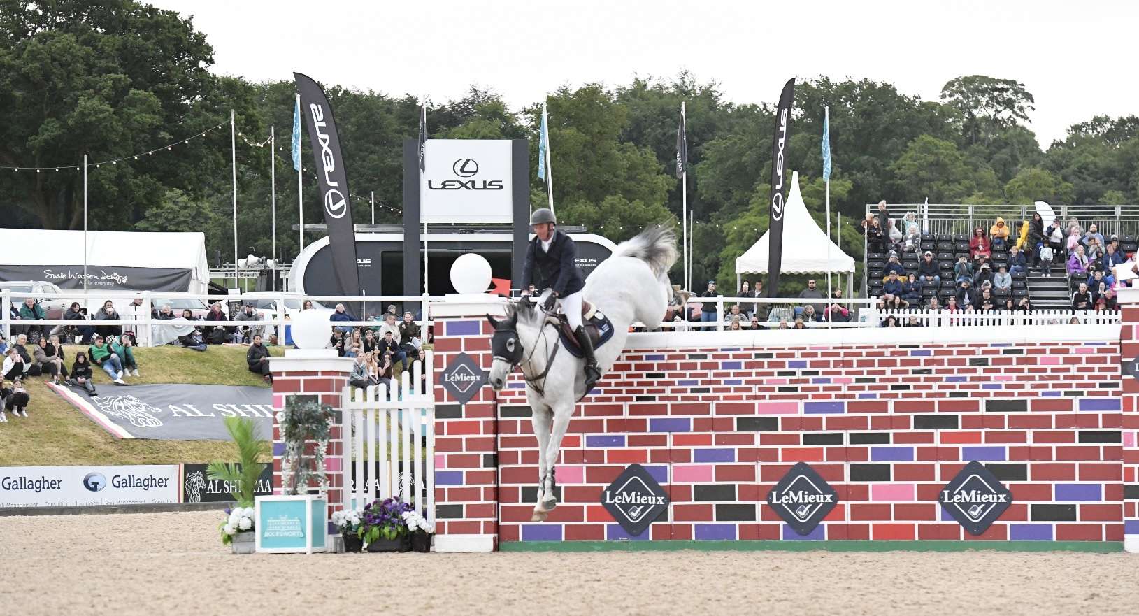 a grey horse jumping a big red brick wall