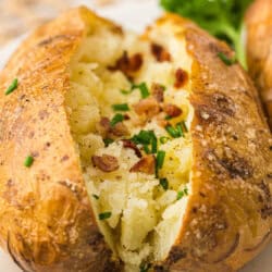 Baked potato garnished with bacon, green onion and a sprig of parsley on a white plate and rattan placemat.