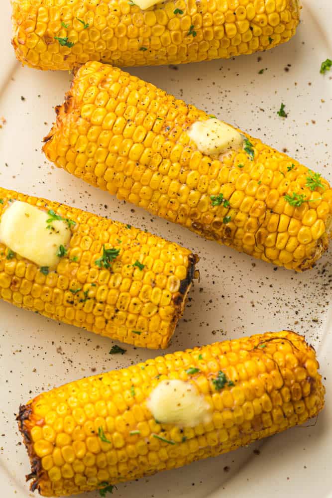 Air fried corn on the cob garnished with parsley and butter on white serving plate.