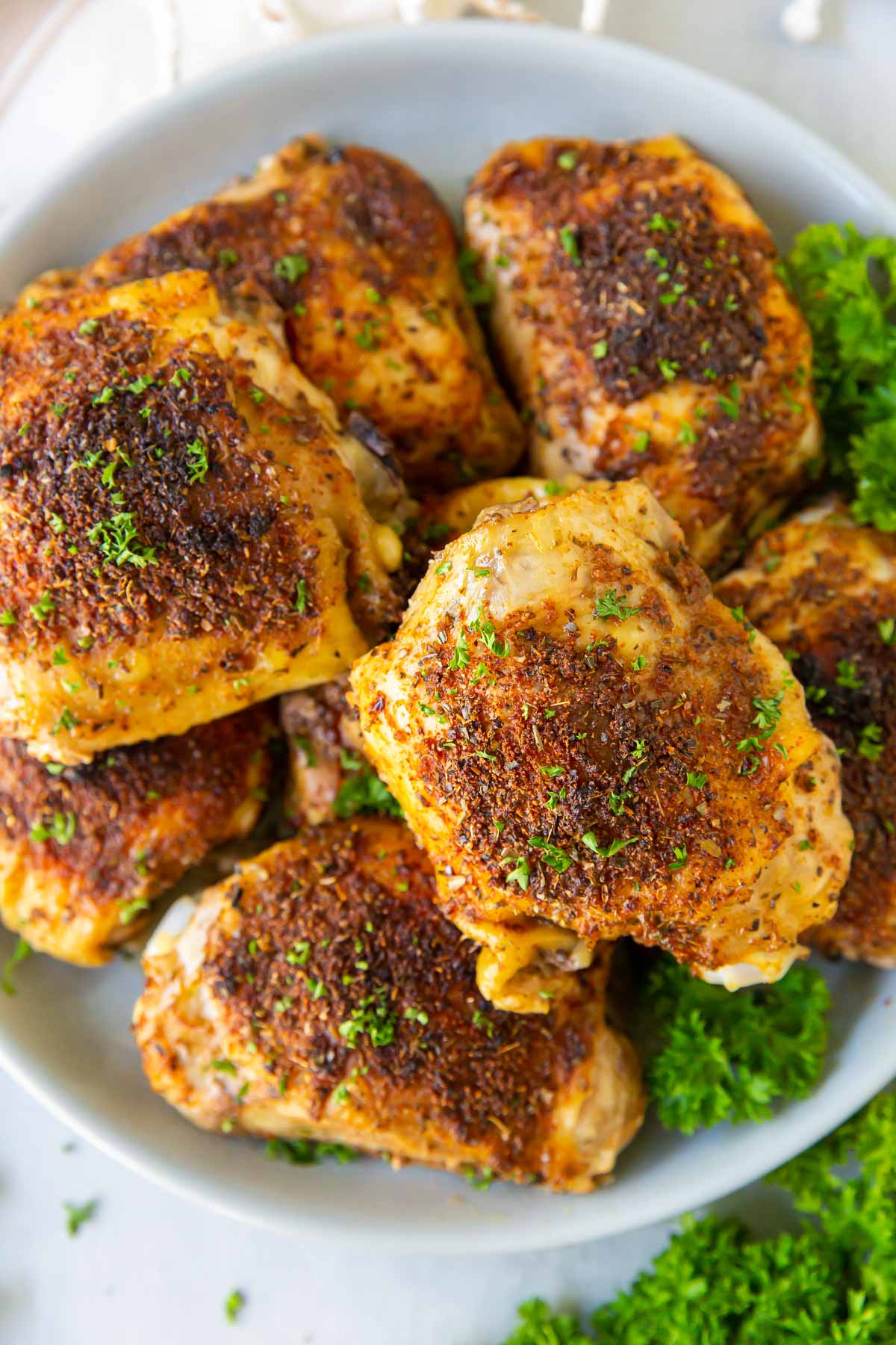 Eight baked bone in chicken thighs stacked on a plate.