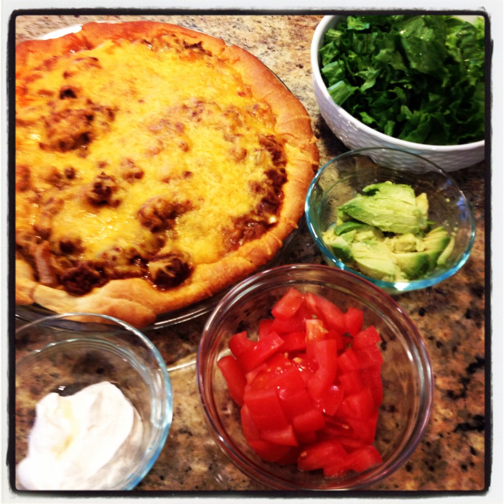 Taco pie covered in melted cheese and veggies on the side.