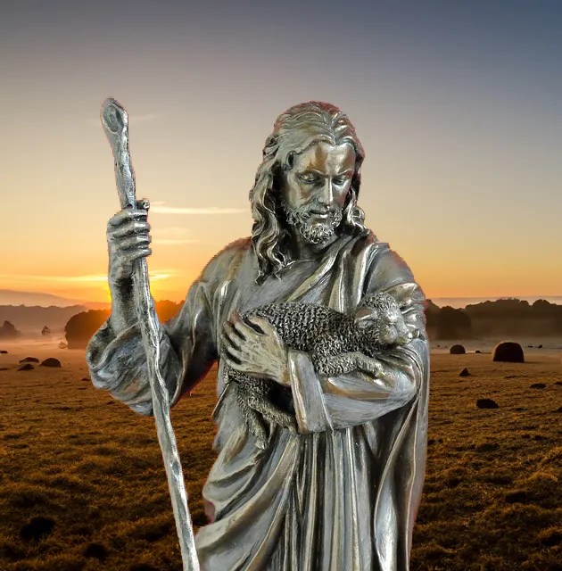 Statue of Jesus holding a lamb, sheep pasture in background