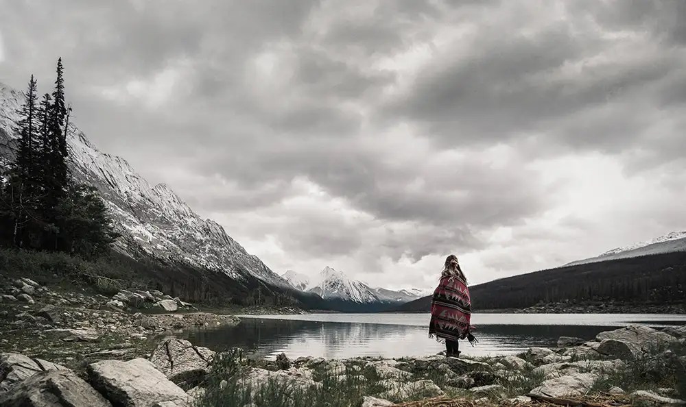 Woman standing in front of a lake, storm clouds covering the sky.