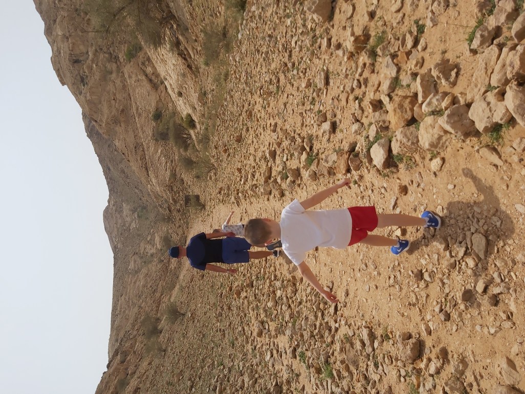 Dad and boy walking on rocky path on family hike in UAE.