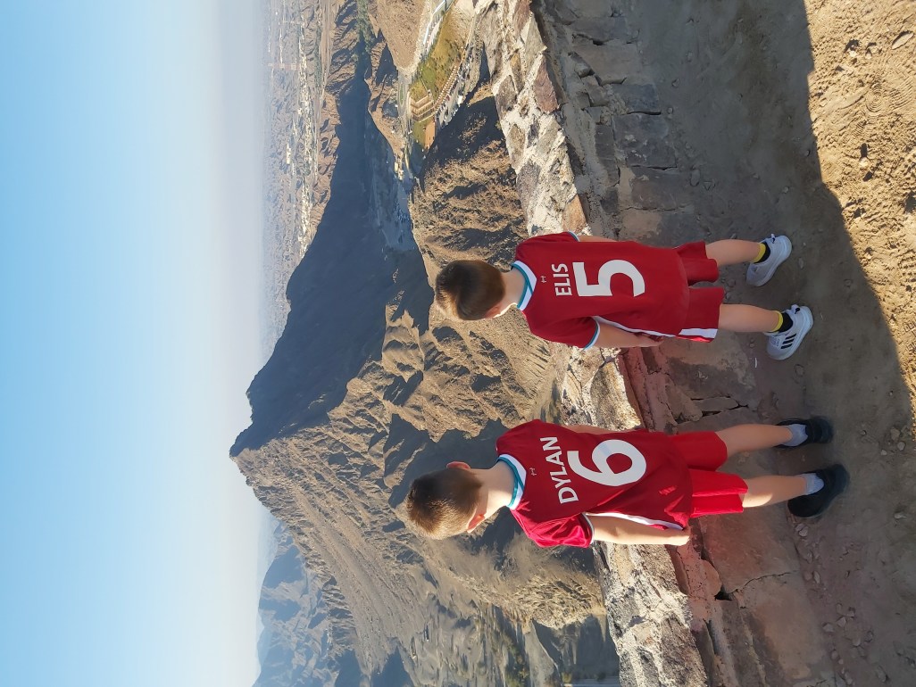 Young boys with 'Dylan' and 'Elis' on the back of their shirts looking at the rocky, mountain view on a family hike in UAE.