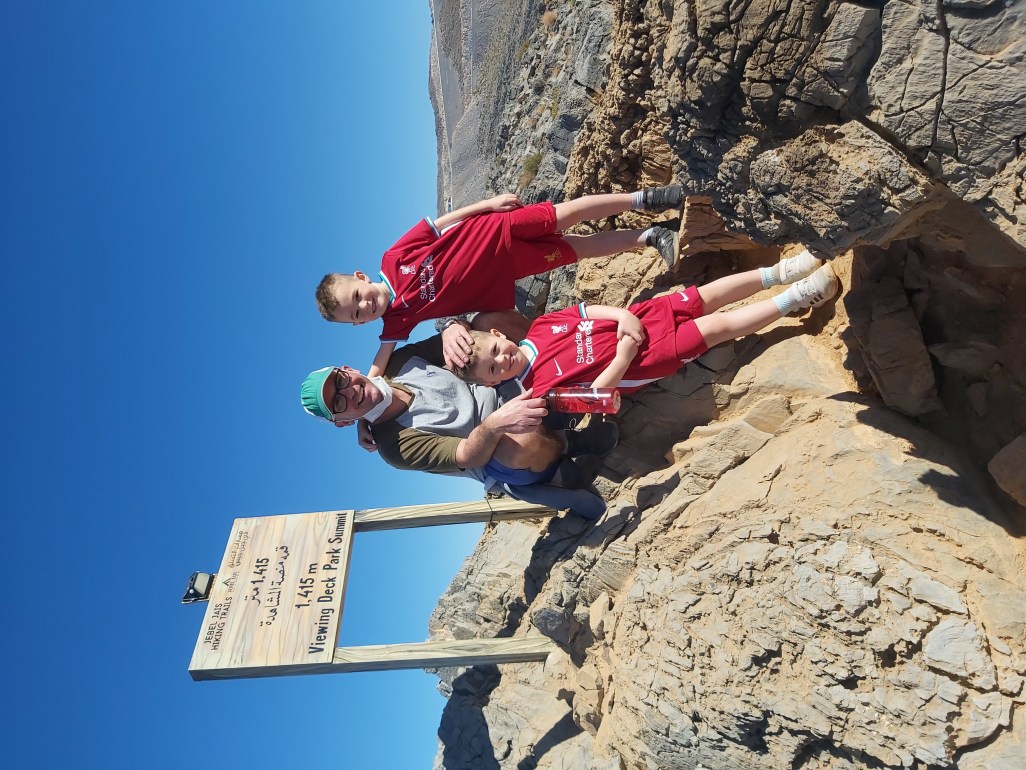 Dad and boys on top of a mountain, smiling, after finishing a family hike in the UAE.