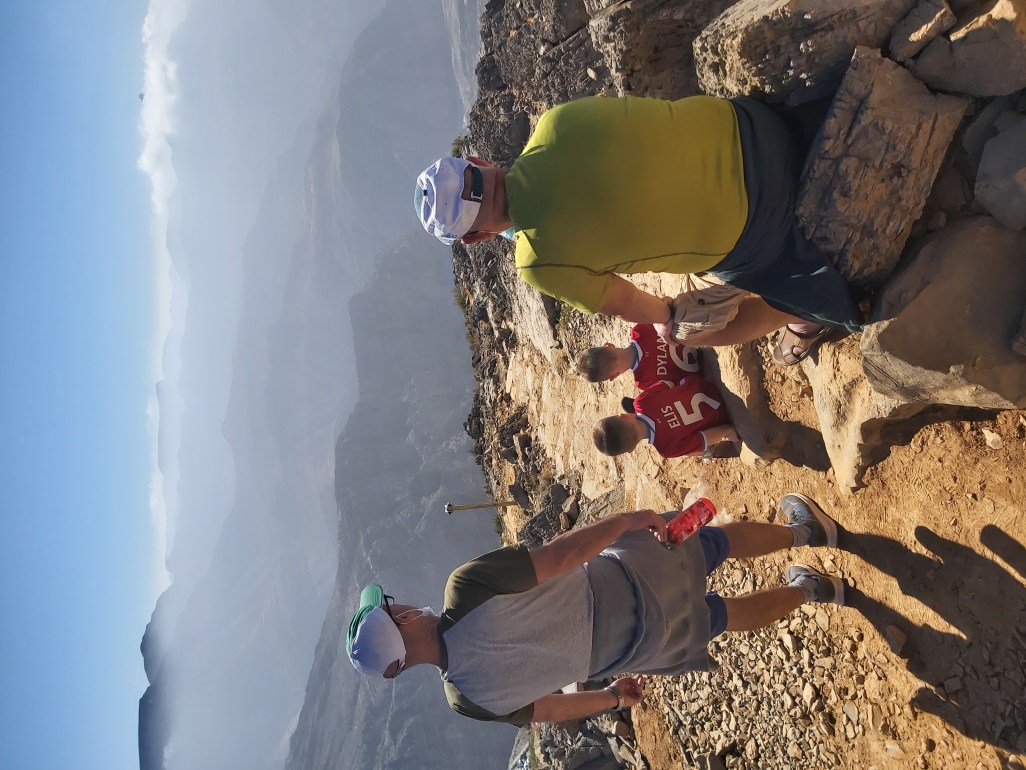 Grandad, Dad and 2 boys looking down on mountain view on family hike in UAE.