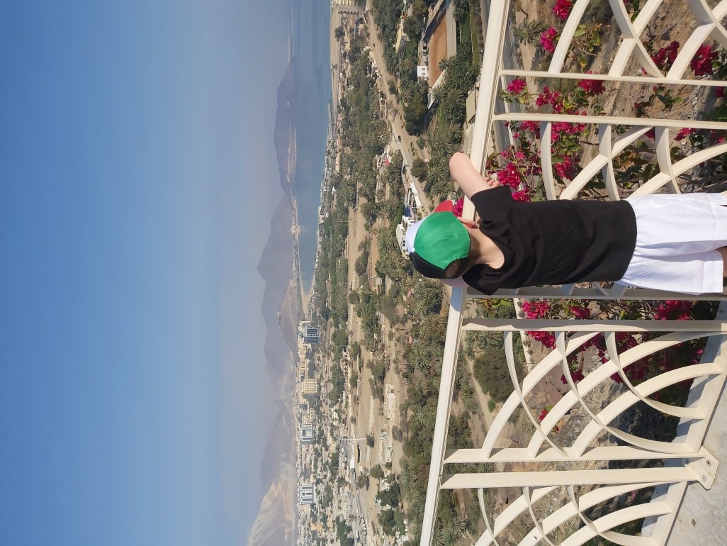 Boy looking down over a town and the ocean at the start of a family hike in UAE.