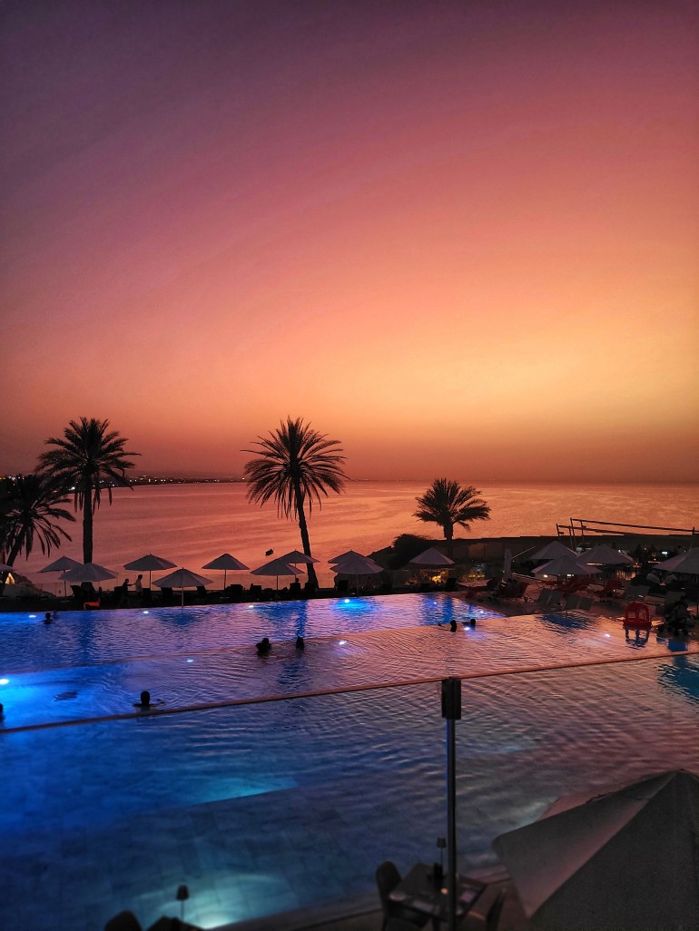 Pink, red and orange sunset sky over an infinity pool and the sea. A perfect dinner spot during a weekend in Muscat. 