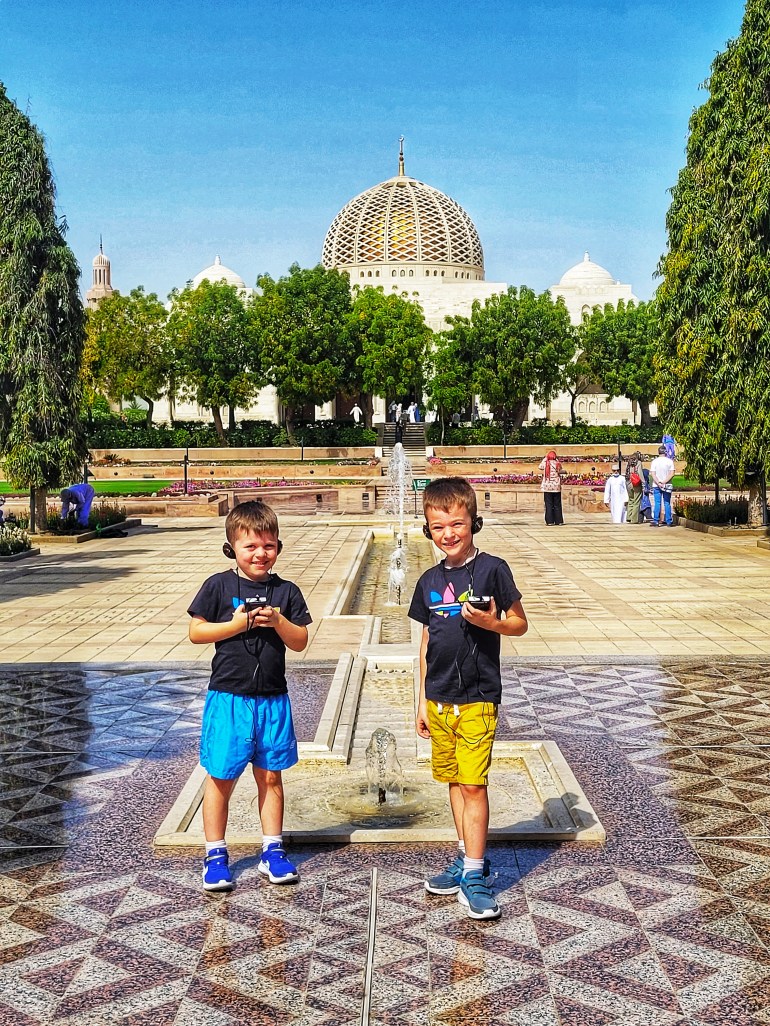 2 boys with headphones listening to explanations of the Sultan Qaboos Grand Mosque during a weekend in Muscat. 