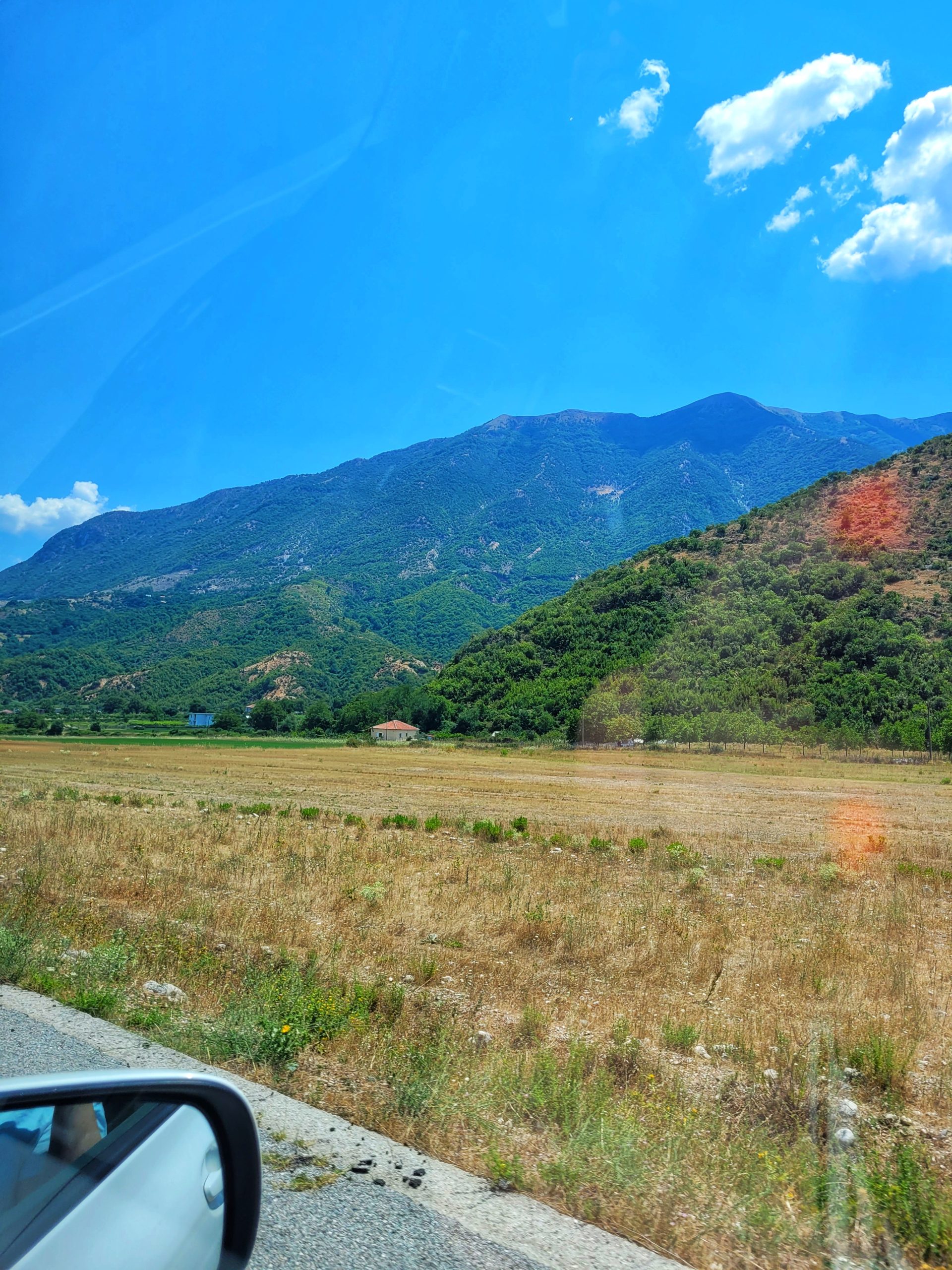 Wing mirror looking out to mountains and grass of the Albanian countryside. Enjoy the countryside on your holiday to Albania. 