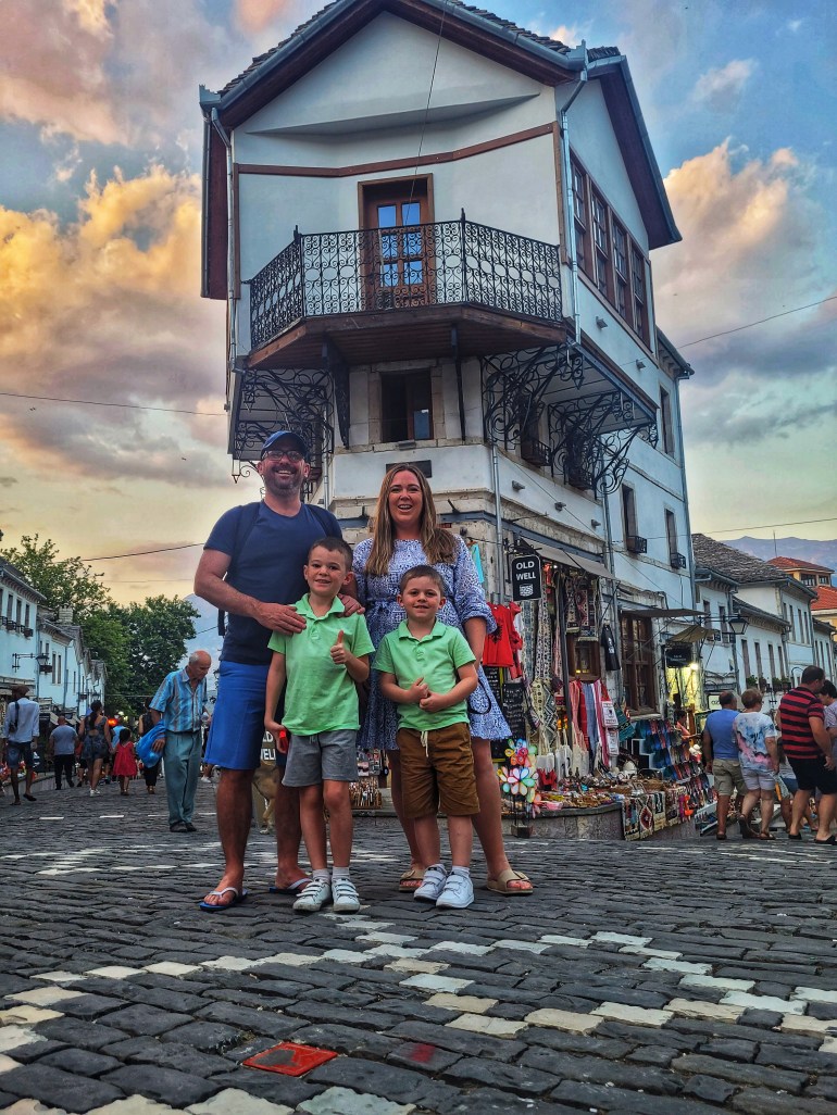 Family picture Mum and 2 boys outside a traditional Albanian shop and house on travel to Albania. 