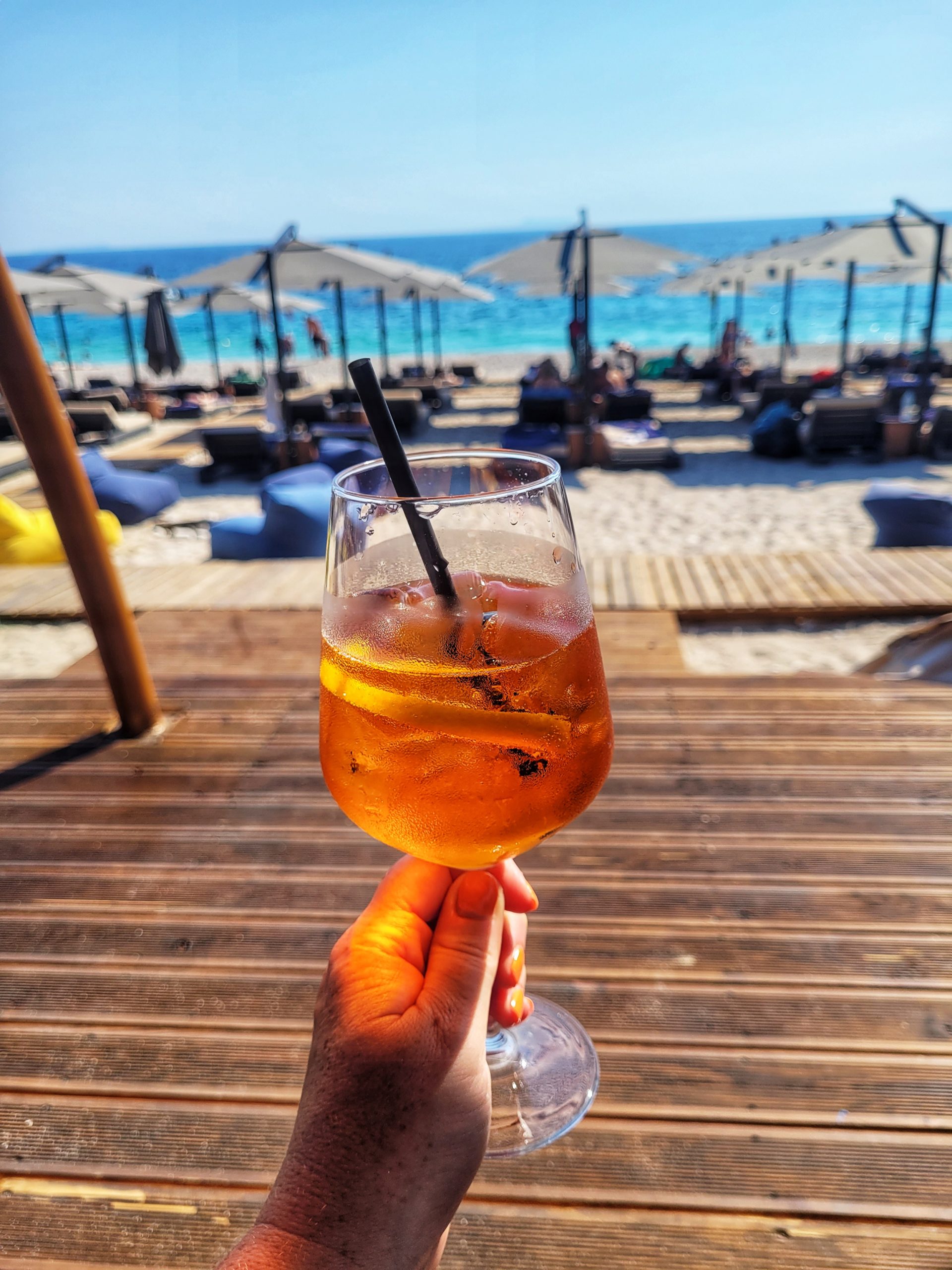 An aperol spritz with the beach and ocean in the background. 