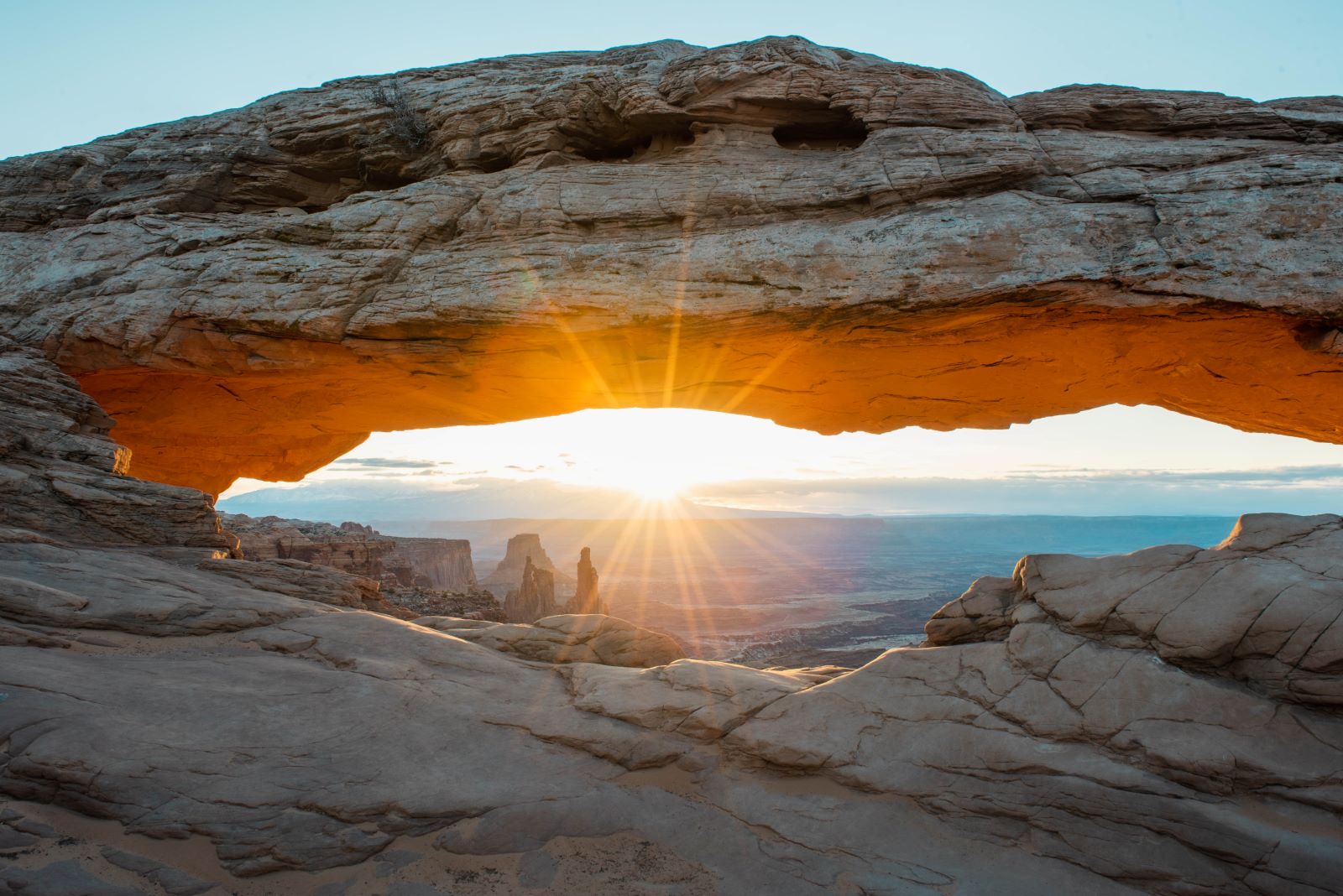 Mesa arch at sunrise glowing red with sun starburst