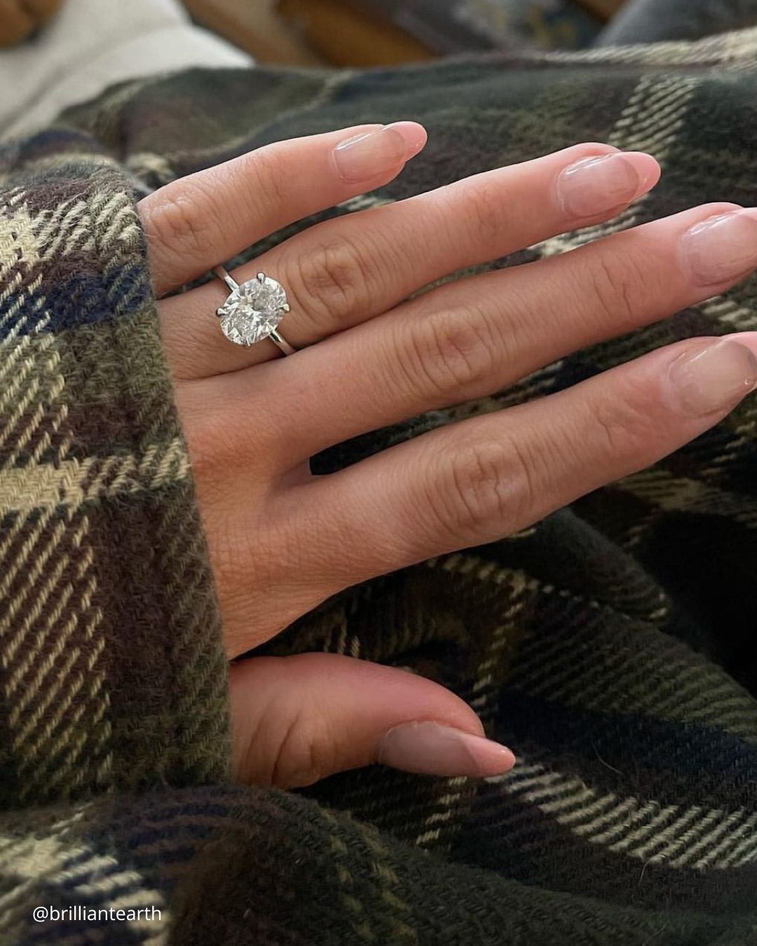 engagement ring designers wedding ring with a big oval center stone on the hand of a girl in a checkered shirt