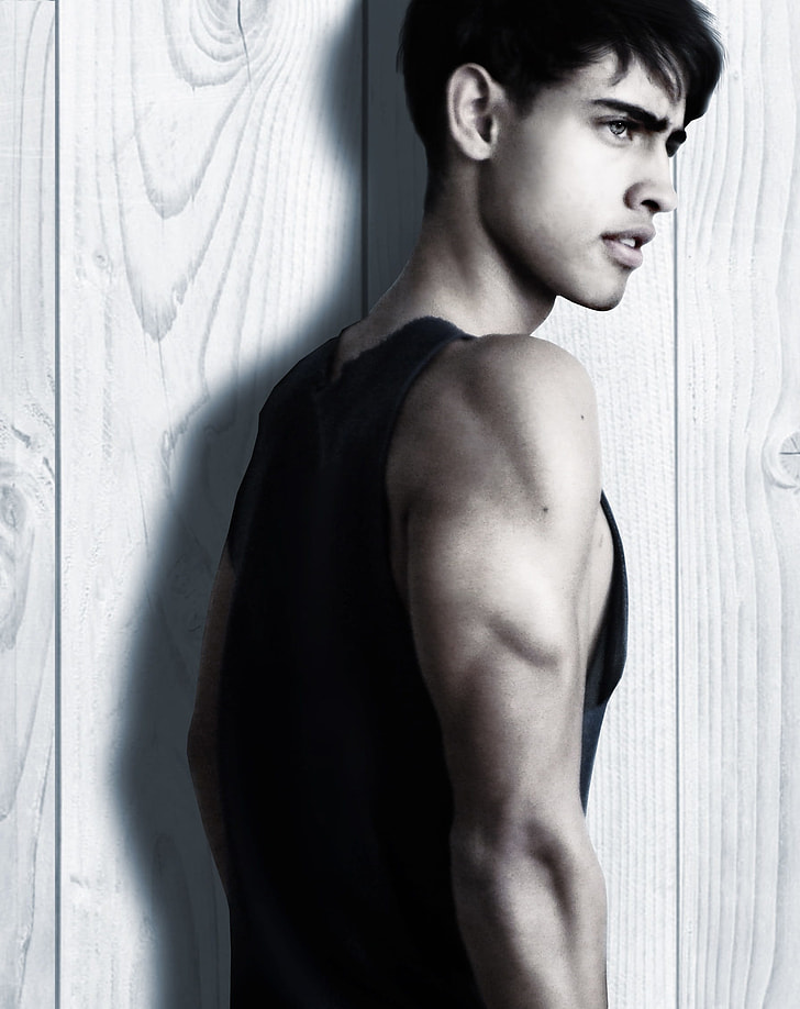 man wearing black tank top beside wooden wall