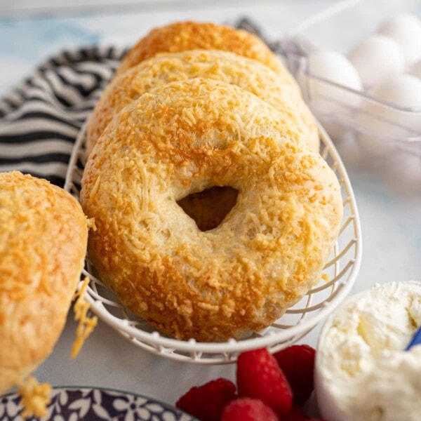 asiago cheese bagels in a wire basket next to a black and white striped dishtowel.