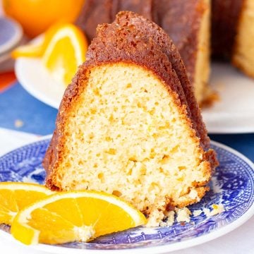 A slice of moist bundt cake on a blue and white plate, garnished with fresh orange slices.