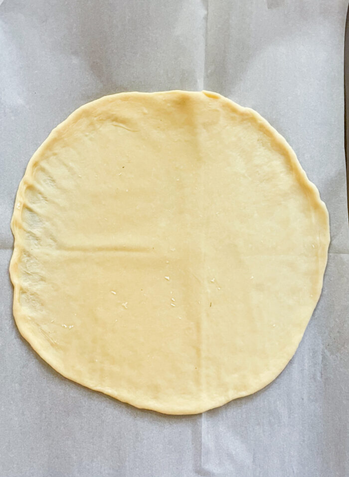 a dough ball rolled into a circle on parchment paper