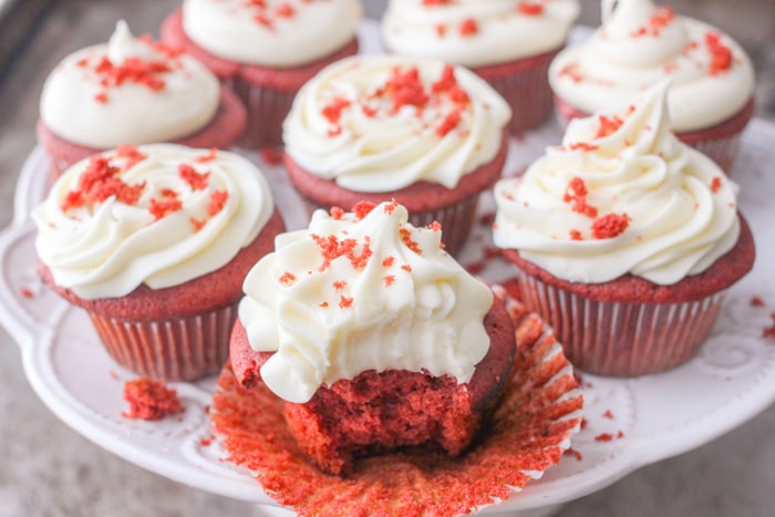 Red velvet cupcakes beautifully decorated with cream cheese frosting on a plate, one with bite taken out