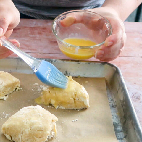 Brushing egg wash on top of a scone with a pastry brush