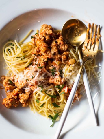 Chicken bolognese served on a pasta plate topped with parmesan cheese.