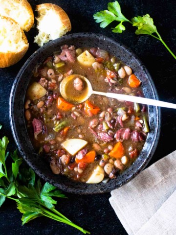 A bowl of crockpot 15 bean soup served with bread and garnished with parsley.