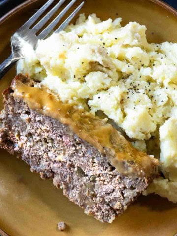 A slice of BBQ meatloaf plated with mashed potatoes.