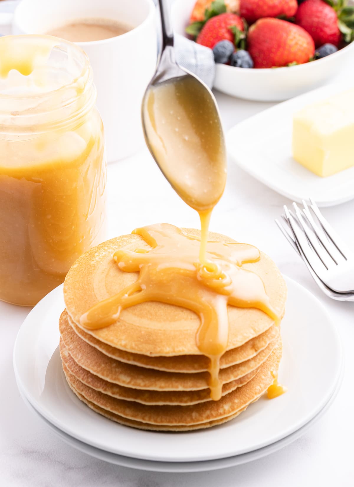 A spoon drizzling buttermilk syrup over the top of a stack of pancakes.