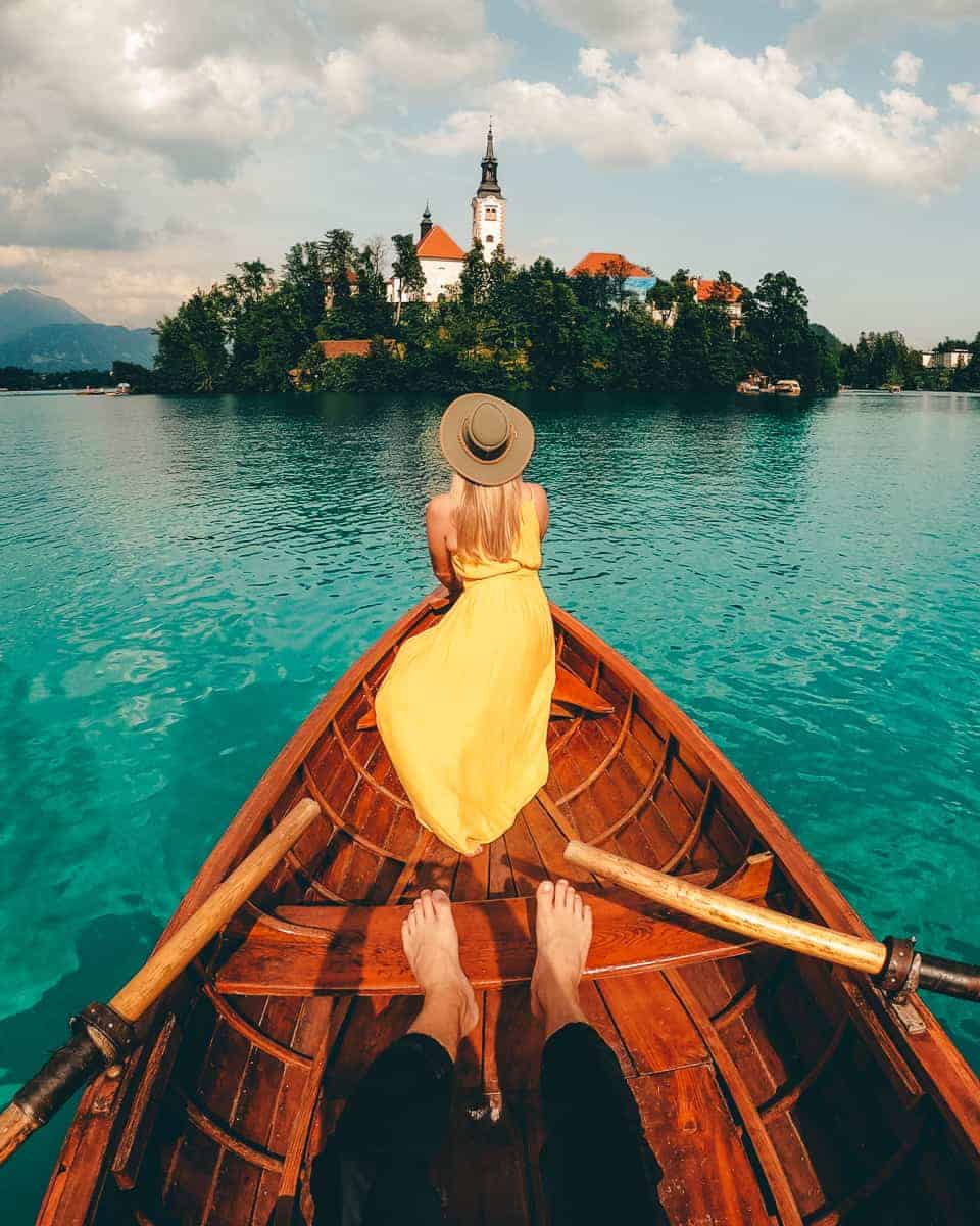 Girl in yellow dress in a row boat facing Bled Island