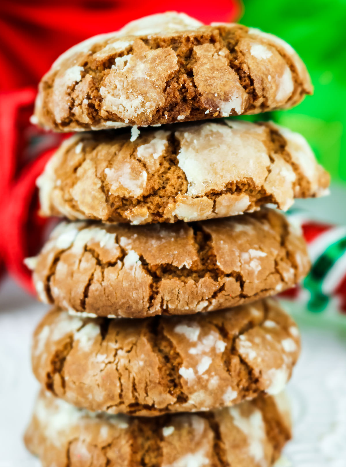 Closeup on a stack of Gingerbread Crinkle Cookies sitting on a white table in front of Christmas decorations.