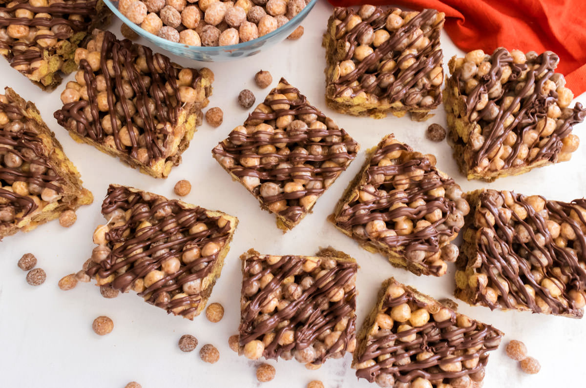 Overhead shot on a batch of Reese's Puffs Marshmallow Treats laying on a white table surrounded by cereal and an orange kitchen towel.