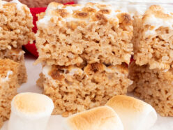 A batch of Toasted Marshmallow Rice Krispie Treats sitting on a white table surrounded by roasted marshmallows.