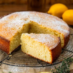 Olive Oil Cake on a rack on a wooden table with a piece cut.