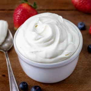 Bowl of Whipped Cream Cheese Frosting on a wooden table close up.