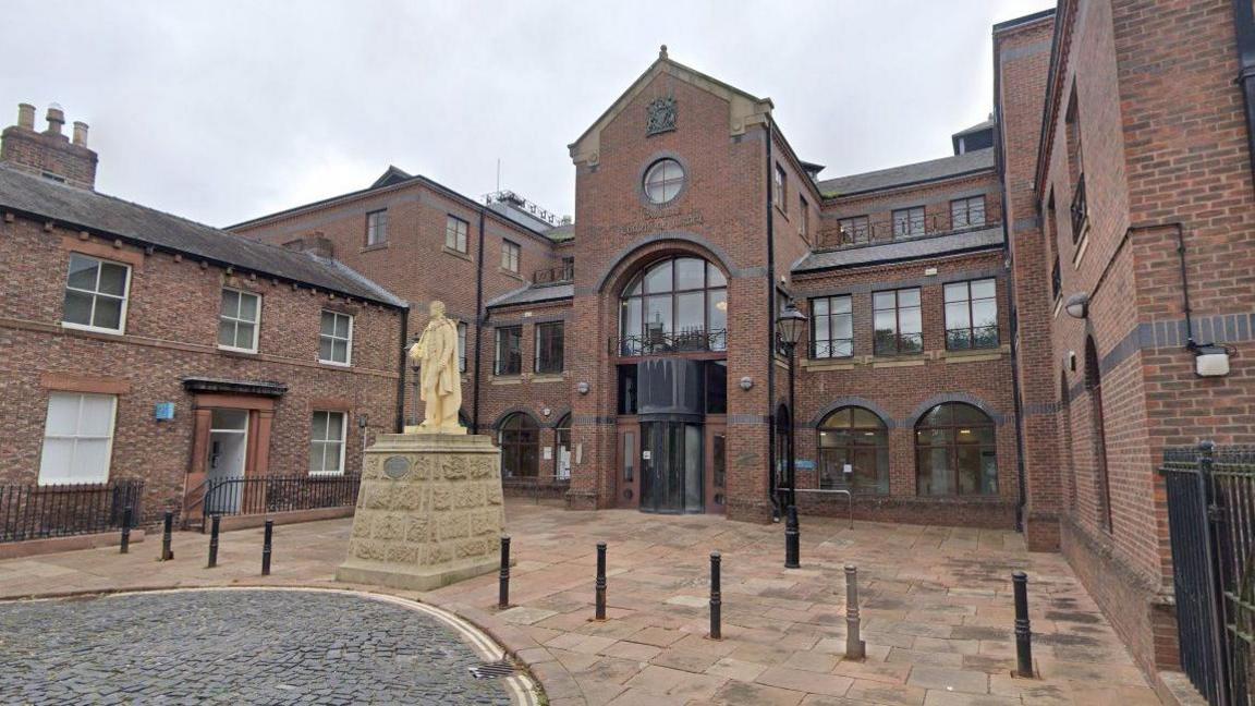 A general street view of the front of the Carlisle Crown Court building. There is a statue outside.