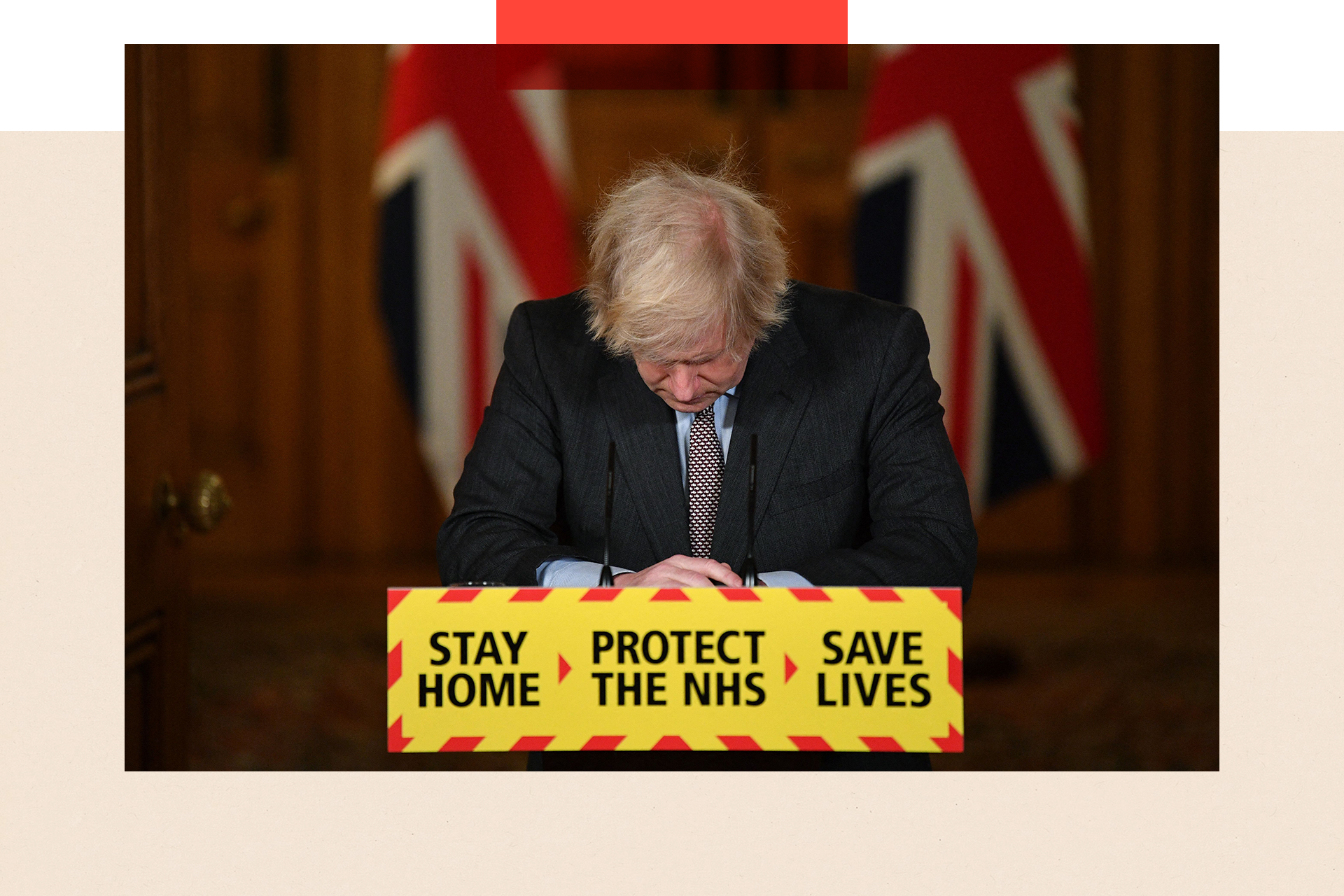 Boris Johnson looks down at the podium as he attends a virtual press conference on the Covid-19 pandemic, the slogan on the stage reads 'stay home, protect the NHS, save lives'