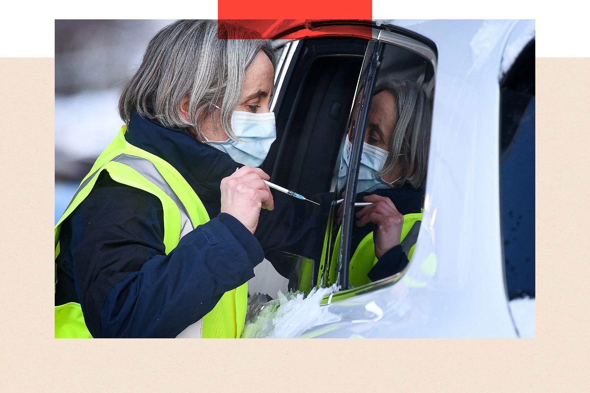 A member of staff administers a COVID-19 vaccine to a member of the public through a car window of the public