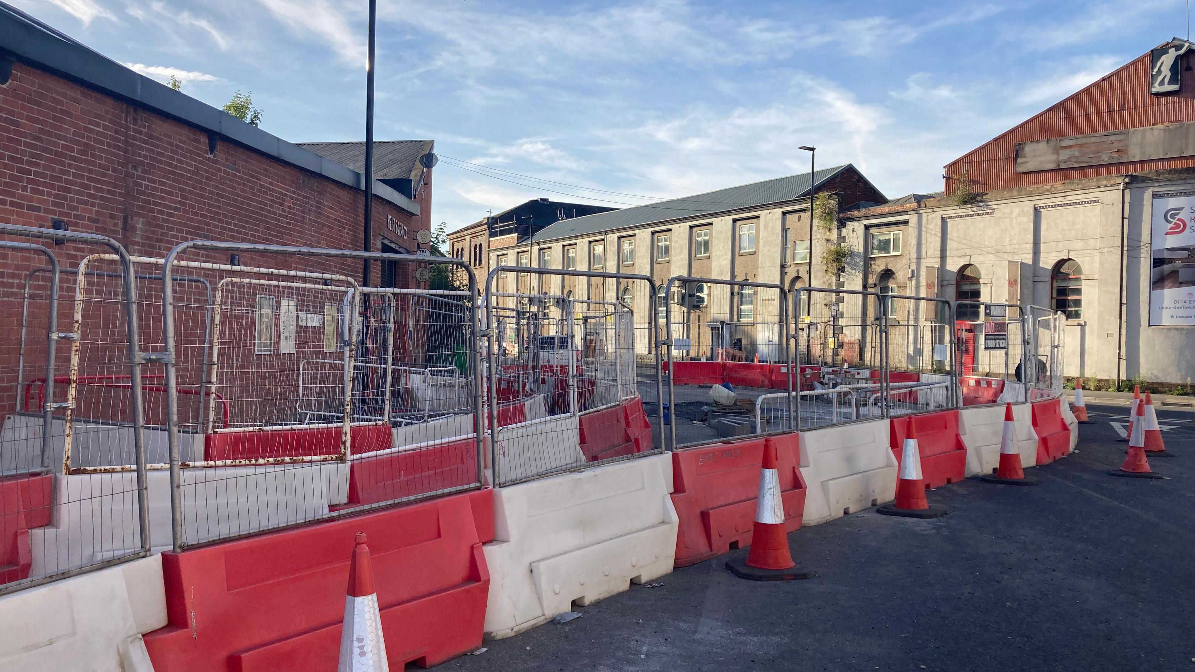 Red and white roadworks barriers along with fencing are erected along the road. Traffic cones are dotted alongside it.