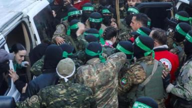 Doron Steinbrecher walks through a crowd of Hamas fighters, with their faces covered and wearing green bandanas, and Emily Damari gets out of a vehicle as both women are handed over to the Red Cross