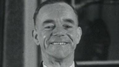 A screenshot from a black and white archive film from 1952.  Albert Gunter is smiling proudly and wearing his bus driver uniform.