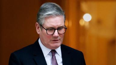 Sir Keir Starmer wearing dark suit and glasses away from camera as he steps out of the front door at Number 10, in London on 14 January